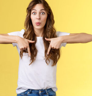 Fascinated impressed charismatic brunette female curly long haircut folding lips whistle astonished react excited thrilled telling you incredible promotion pointing down bottom yellow background.